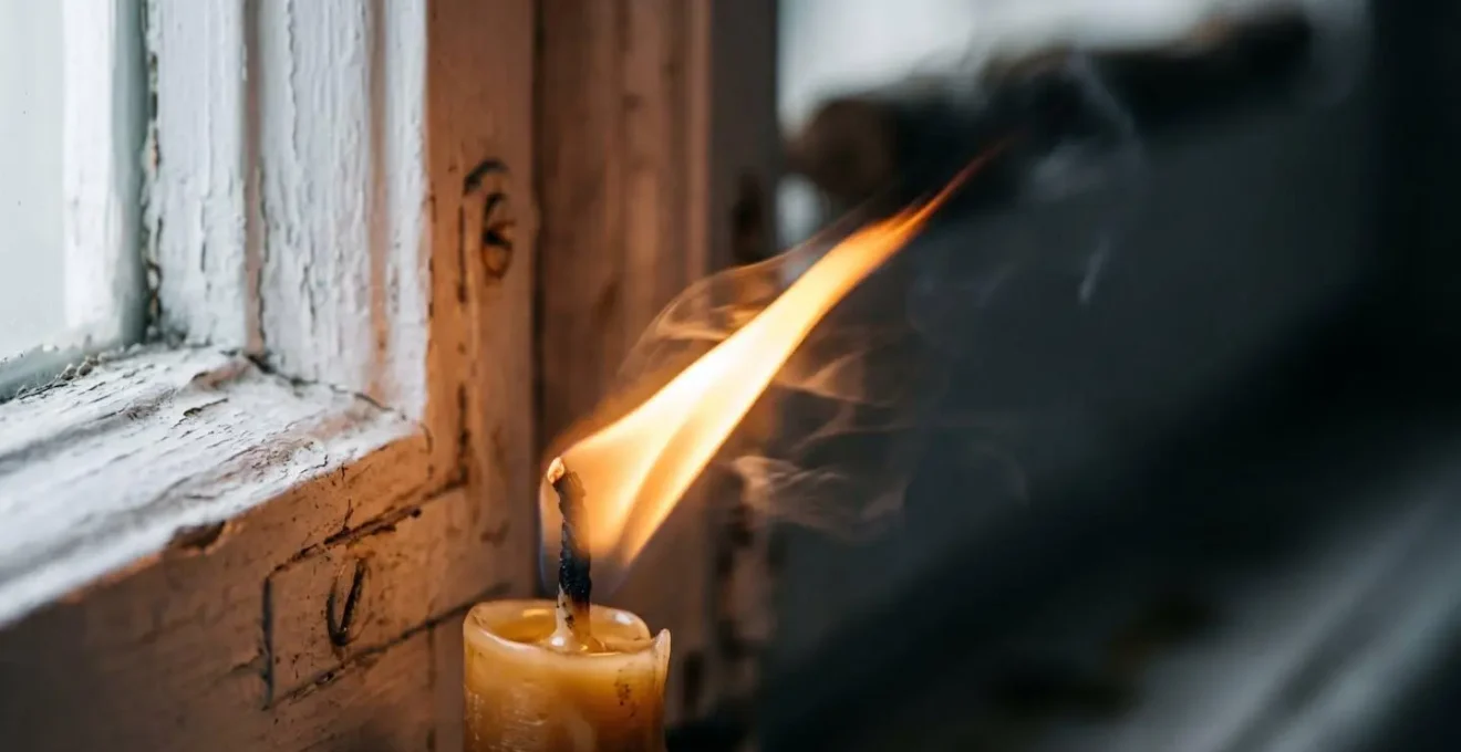 Gros plan sur une flamme de bougie vacillant près d'une jonction de fenêtre révélant un courant d'air invisible