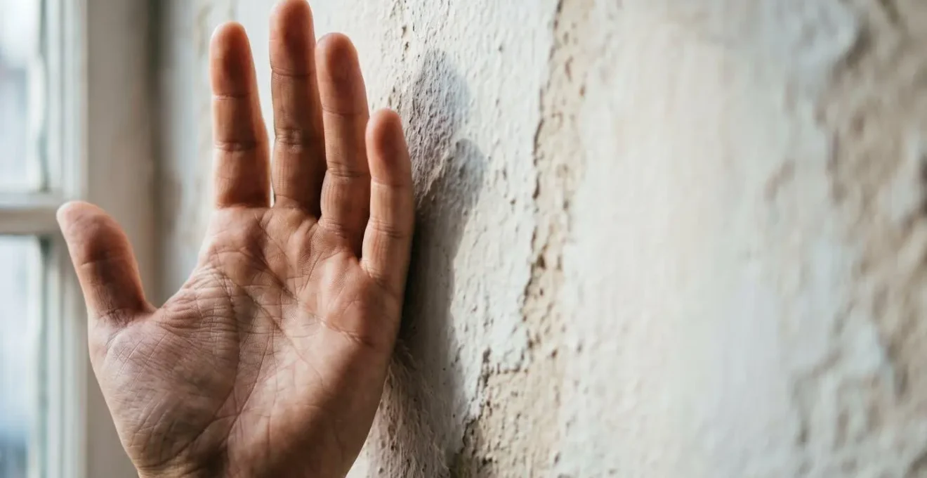 Gros plan sur une main projetant une ombre sur un mur près d'une fenêtre pour diagnostiquer l'intensité lumineuse, technique simple d'évaluation de l'exposition pour plantes d'intérieur