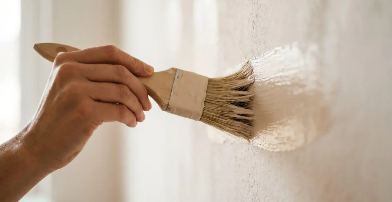 Gros plan artistique sur un pinceau appliquant une peinture écologique beige sur un mur texturé, mouvement délicat illustrant la rénovation saine et responsable